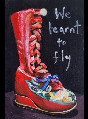 Frida Kahlo's red knee length boot with embroidered yellow flowers and a bell on the front. The laces are from a red ribbon. The boot sits on a black background, to the right is white hand writing that says We learnt to fly